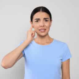 Woman with tinnitus holding her ear and looking uncomfortable.