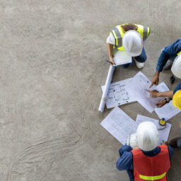 An overhead shot of four people at a construction site, they are all viewing the same document and appear to be discussing building plans